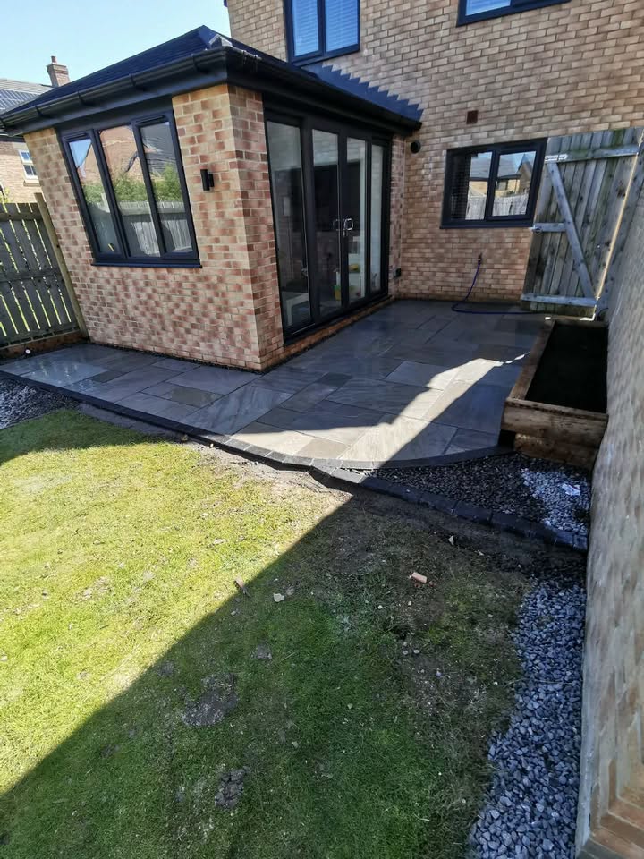 Stone patio wrapping a home extension with lawn and timber planter